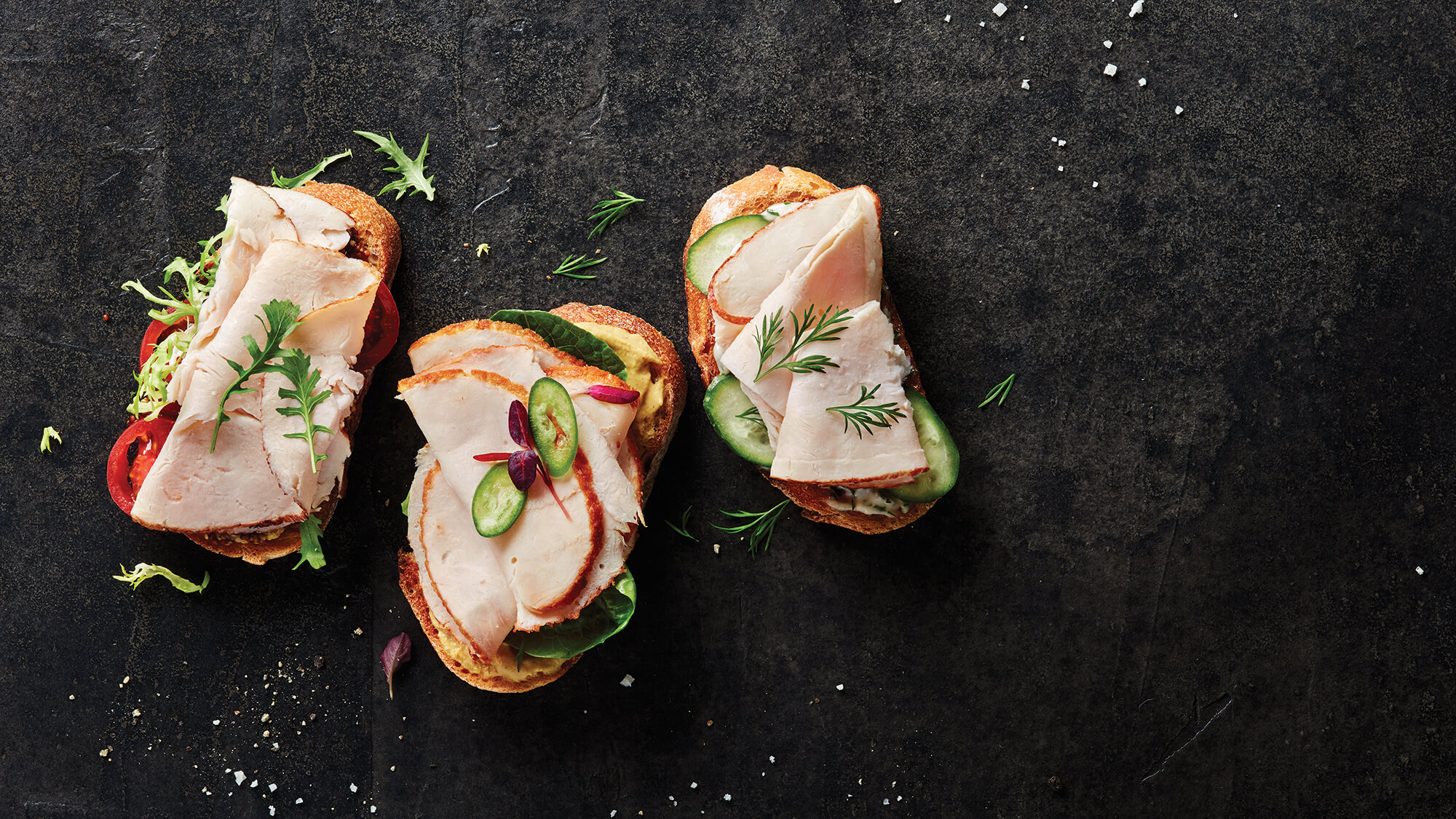 Group of three open-faced Columbus Chicken sandwiches with various toppings on a black slate