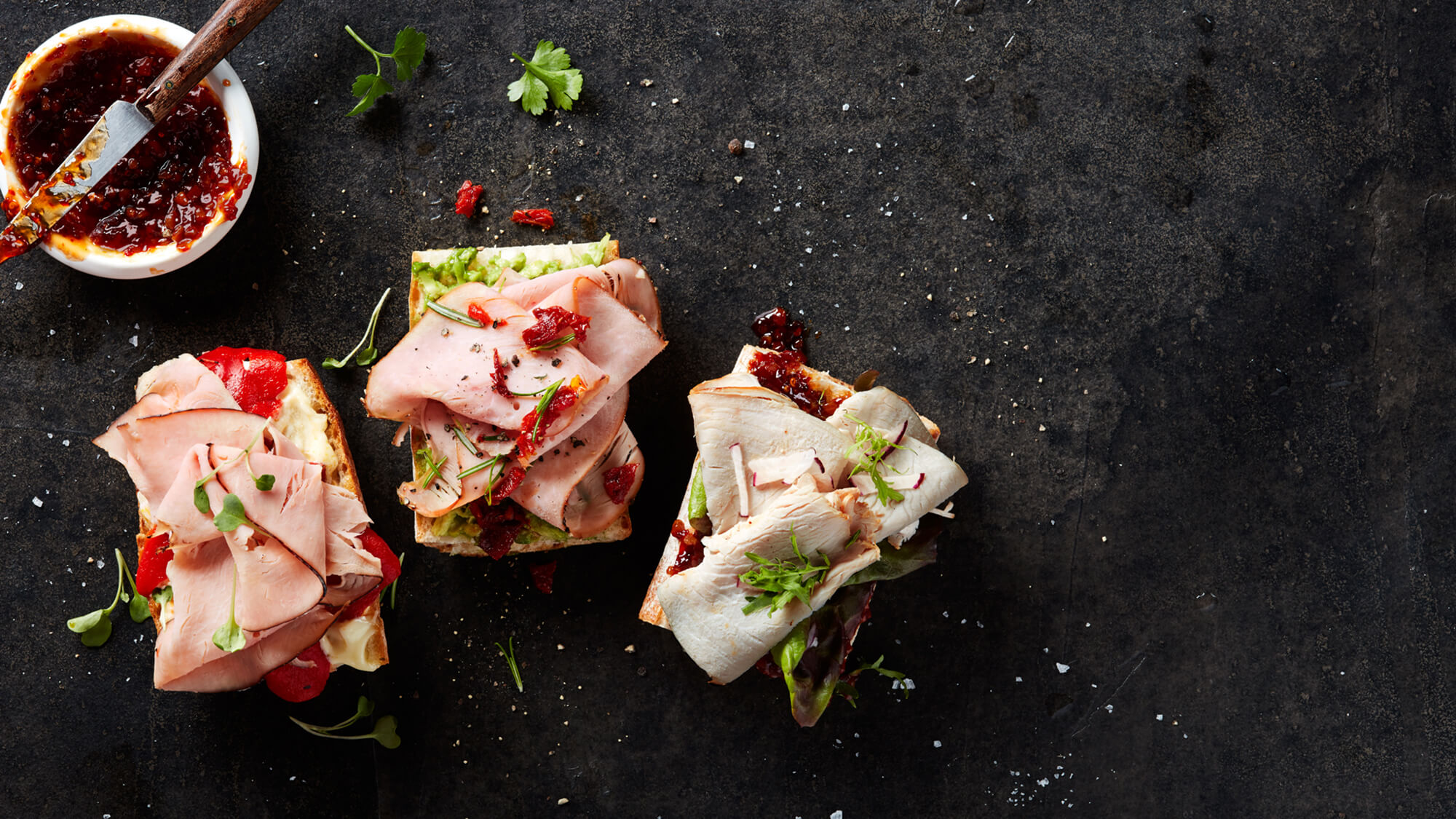 Three open-faced sandwiches made Columbus Turkey and topped with various herbs, cheeses, and dressings