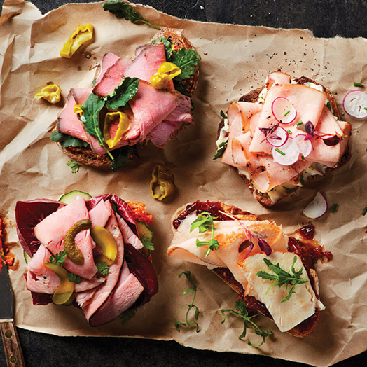 Four open faced deli meat sandwiches made with Columbus Roast Beef, Chicken, Turkey, and Ham on brown butcher paper