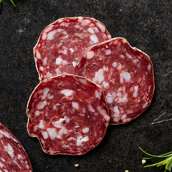 Sliced Columbus Rosette De Lyon Salami on black slate with crushed white peppercorns and a sprig of rosemary